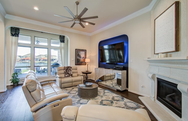 living area with a ceiling fan, baseboards, a fireplace, dark wood-style flooring, and crown molding