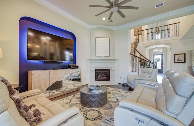 living area featuring visible vents, a ceiling fan, wood finished floors, crown molding, and stairs