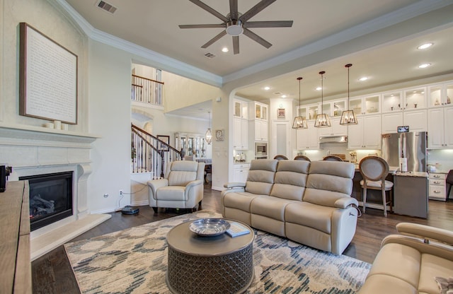 living room featuring dark wood-style floors, ceiling fan, crown molding, and stairway