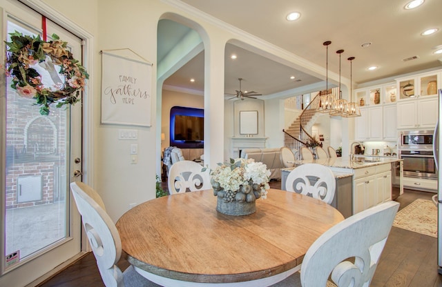 dining area featuring visible vents, arched walkways, dark wood-style flooring, ornamental molding, and ceiling fan