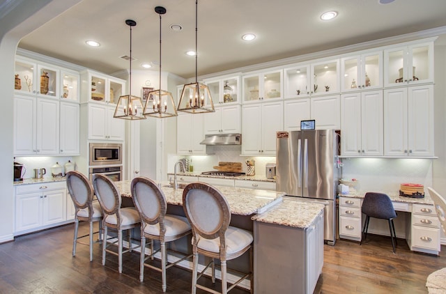 kitchen with an island with sink, under cabinet range hood, dark wood finished floors, appliances with stainless steel finishes, and hanging light fixtures