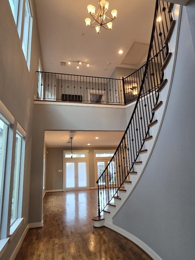 stairs with baseboards, an inviting chandelier, wood finished floors, and a towering ceiling