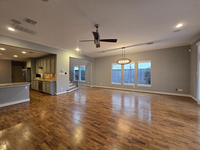 unfurnished living room with visible vents, dark wood-type flooring, a ceiling fan, and crown molding