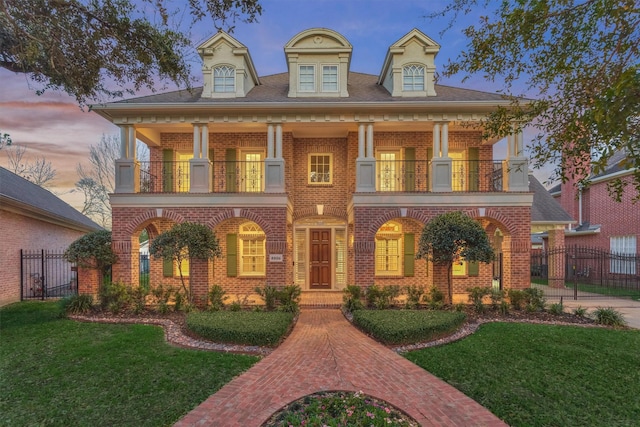 view of front facade with a balcony, a yard, fence, and brick siding