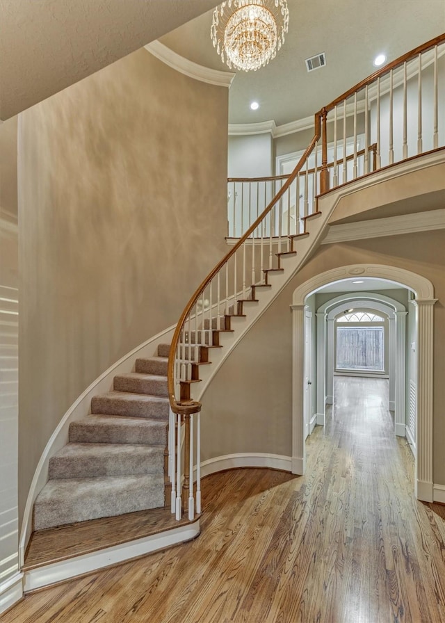 stairway featuring wood finished floors, baseboards, an inviting chandelier, arched walkways, and ornamental molding