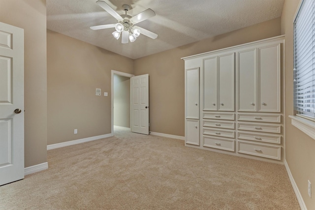 unfurnished bedroom with light carpet, ceiling fan, a textured ceiling, and baseboards