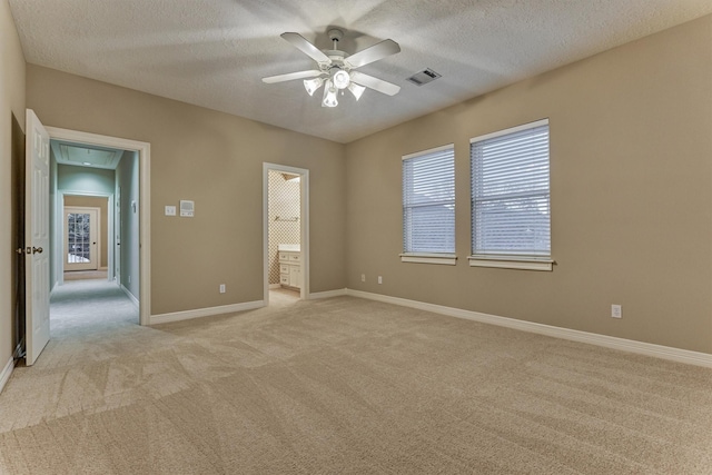 unfurnished bedroom featuring visible vents, baseboards, ensuite bath, a textured ceiling, and light colored carpet