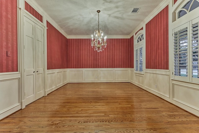 unfurnished dining area with a chandelier, visible vents, wood finished floors, and ornamental molding