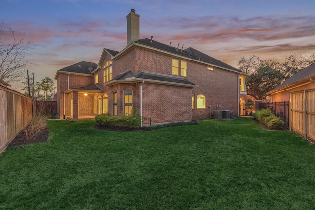 back of property at dusk featuring brick siding, a fenced backyard, a lawn, and central AC