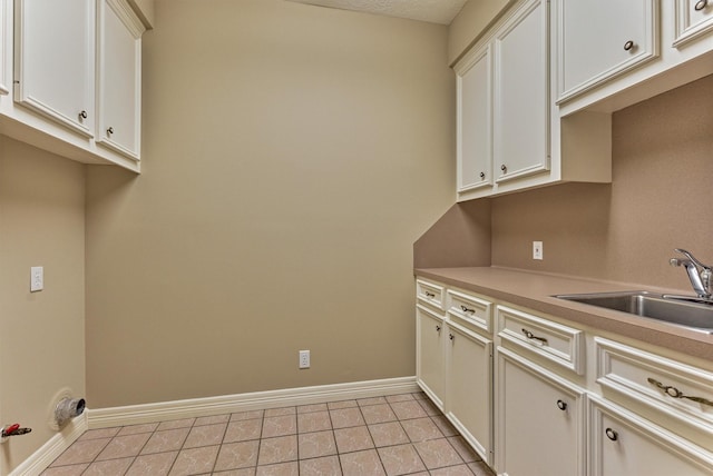 laundry area with light tile patterned floors, cabinet space, baseboards, and a sink