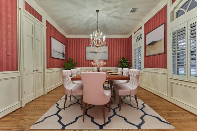 dining area featuring wallpapered walls, crown molding, wainscoting, an inviting chandelier, and wood finished floors