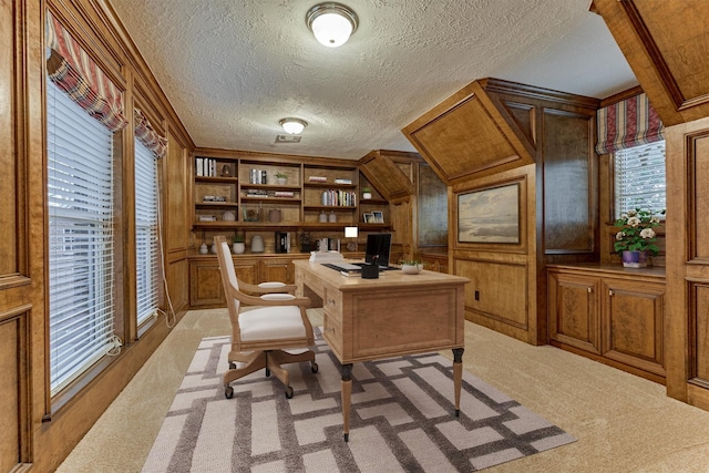 office with wooden walls, light colored carpet, built in shelves, and a textured ceiling