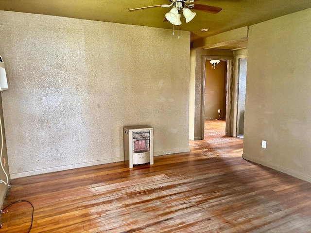 spare room featuring heating unit, wood finished floors, baseboards, and ceiling fan