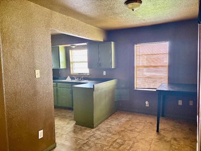 kitchen featuring green cabinets, a peninsula, a sink, and a textured ceiling