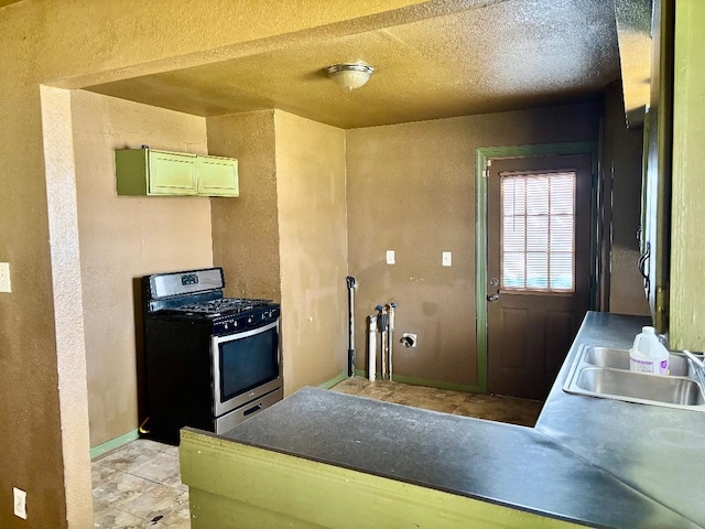 kitchen featuring baseboards, a sink, a textured ceiling, a textured wall, and stainless steel gas stove