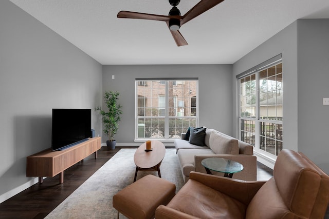 living area featuring dark wood finished floors, baseboards, and ceiling fan