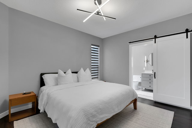 bedroom with connected bathroom, a barn door, baseboards, and dark wood finished floors