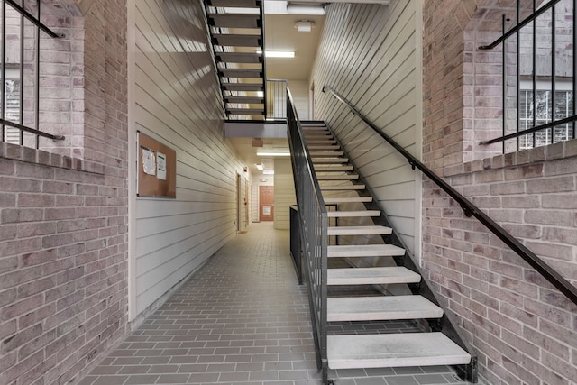 stairway with brick floor, a high ceiling, brick wall, and wooden walls