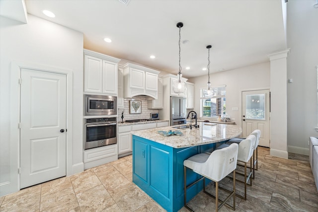 kitchen with an island with sink, a sink, backsplash, white cabinetry, and appliances with stainless steel finishes