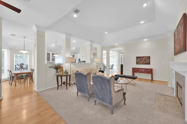 living area featuring visible vents, light wood finished floors, decorative columns, plenty of natural light, and a tiled fireplace