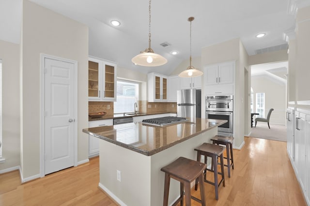 kitchen featuring a kitchen bar, appliances with stainless steel finishes, white cabinets, glass insert cabinets, and lofted ceiling