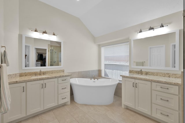 bathroom featuring vaulted ceiling, a freestanding tub, two vanities, and a sink