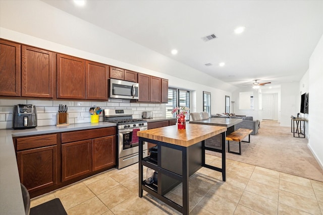 kitchen featuring light tile patterned floors, visible vents, stainless steel appliances, light colored carpet, and backsplash