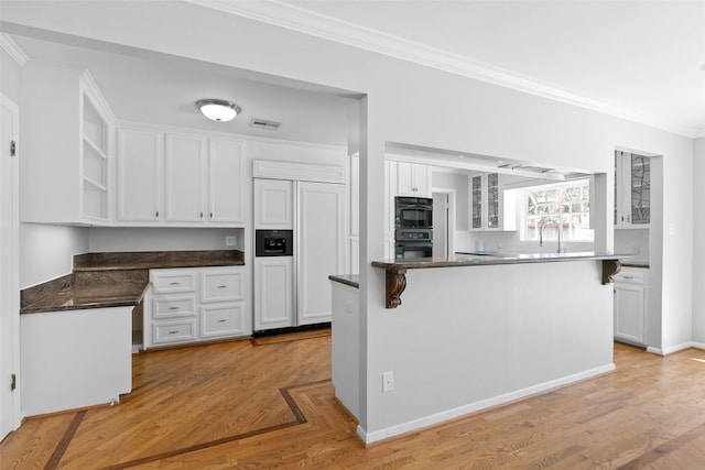 kitchen featuring paneled built in fridge, dark countertops, crown molding, and white cabinetry