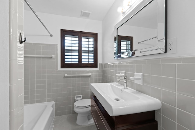 bathroom with visible vents, toilet, wainscoting, tile patterned floors, and tile walls