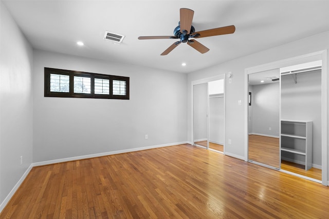 unfurnished bedroom with recessed lighting, wood finished floors, visible vents, and two closets