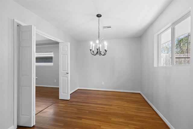 unfurnished dining area with a chandelier, visible vents, baseboards, and wood finished floors