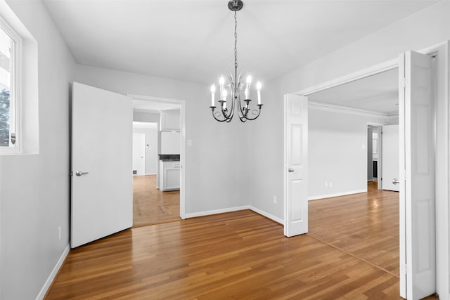 unfurnished dining area with baseboards, a notable chandelier, and light wood finished floors