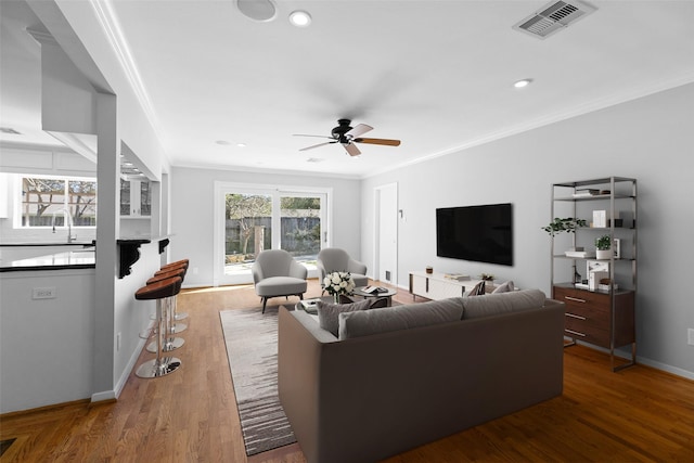 living room with visible vents, wood finished floors, crown molding, baseboards, and ceiling fan