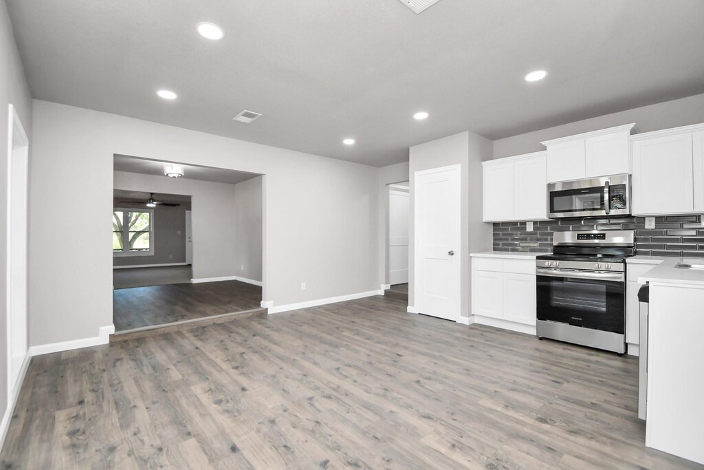 142 County Road 2273, Cleveland, TX 77327 - kitchen with backsplash, stainless steel appliances, light wood-style floors, white cabinets, and light countertops