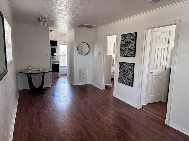 corridor with visible vents, a textured ceiling, dark wood-type flooring, and ornamental molding