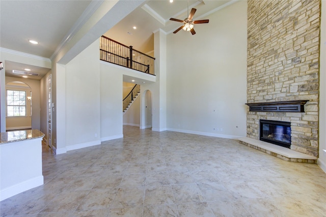 unfurnished living room with a ceiling fan, baseboards, a fireplace, ornamental molding, and stairs