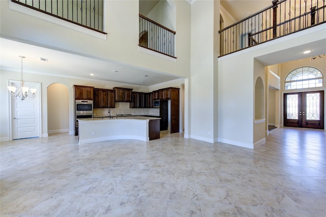 unfurnished living room featuring crown molding, baseboards, french doors, an inviting chandelier, and arched walkways