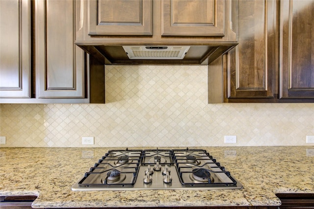 kitchen with range hood, light stone counters, stainless steel gas cooktop, decorative backsplash, and dark brown cabinetry