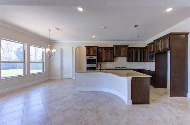 kitchen featuring visible vents, decorative backsplash, an inviting chandelier, stainless steel appliances, and a kitchen island with sink