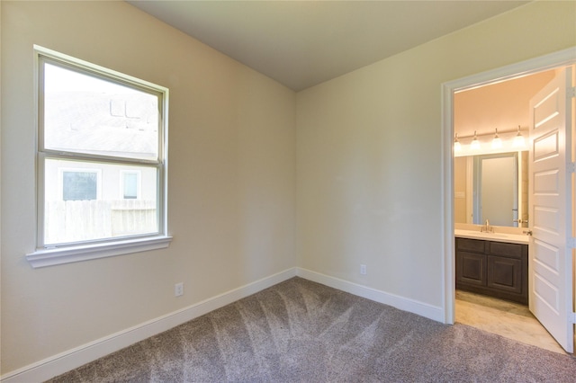 unfurnished bedroom with ensuite bath, light colored carpet, baseboards, and a sink