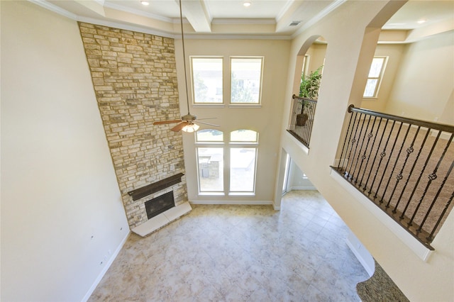 unfurnished living room with a stone fireplace, a ceiling fan, a wealth of natural light, and ornamental molding