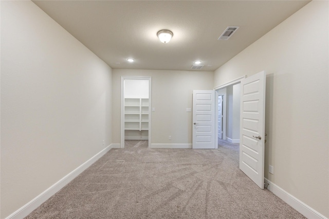 unfurnished bedroom with a spacious closet, visible vents, baseboards, light carpet, and recessed lighting