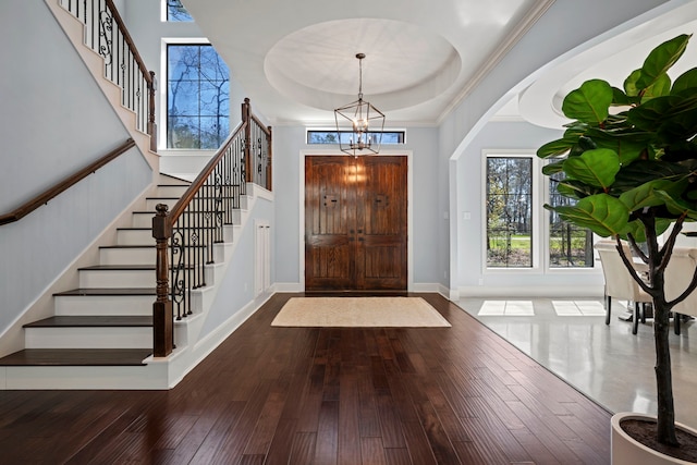 entrance foyer featuring baseboards, ornamental molding, stairs, wood-type flooring, and a notable chandelier