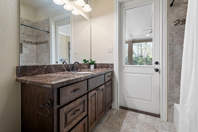 full bathroom featuring tiled shower, vanity, and a textured wall