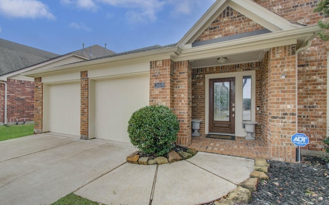 entrance to property featuring concrete driveway, an attached garage, brick siding, and roof with shingles