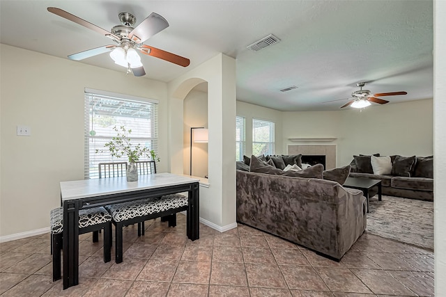 living area with visible vents, arched walkways, a fireplace, and a ceiling fan