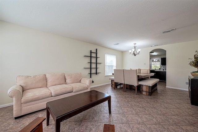 living room with a notable chandelier, arched walkways, visible vents, and baseboards