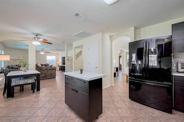 kitchen featuring arched walkways, black fridge with ice dispenser, light countertops, and ceiling fan