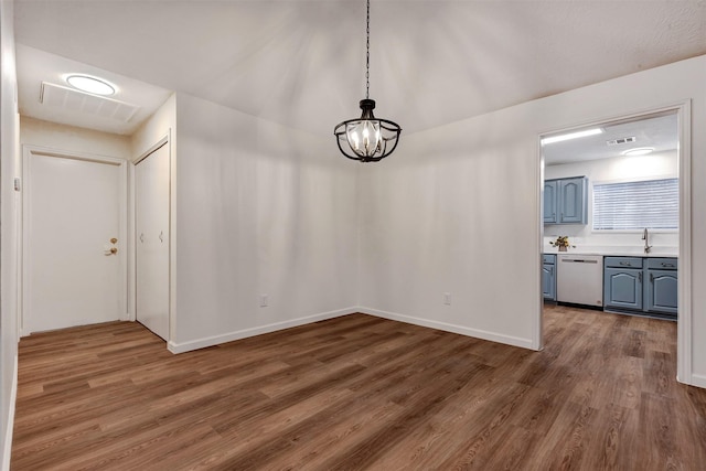 unfurnished dining area with a notable chandelier, a sink, visible vents, and wood finished floors