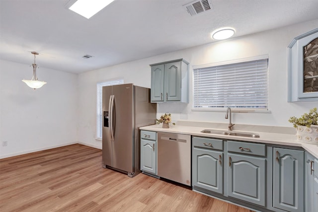 kitchen with light wood finished floors, visible vents, gray cabinetry, stainless steel appliances, and a sink